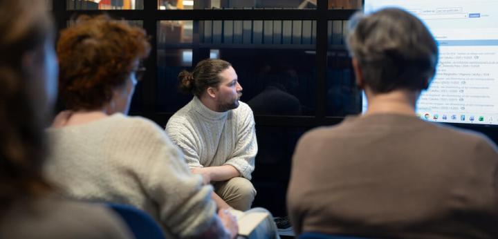 Afbeelding van een workshop, twee deelnemers op de rug bezien en een medewerker van de KB aan het woord naast een PowerPoint-presentatie